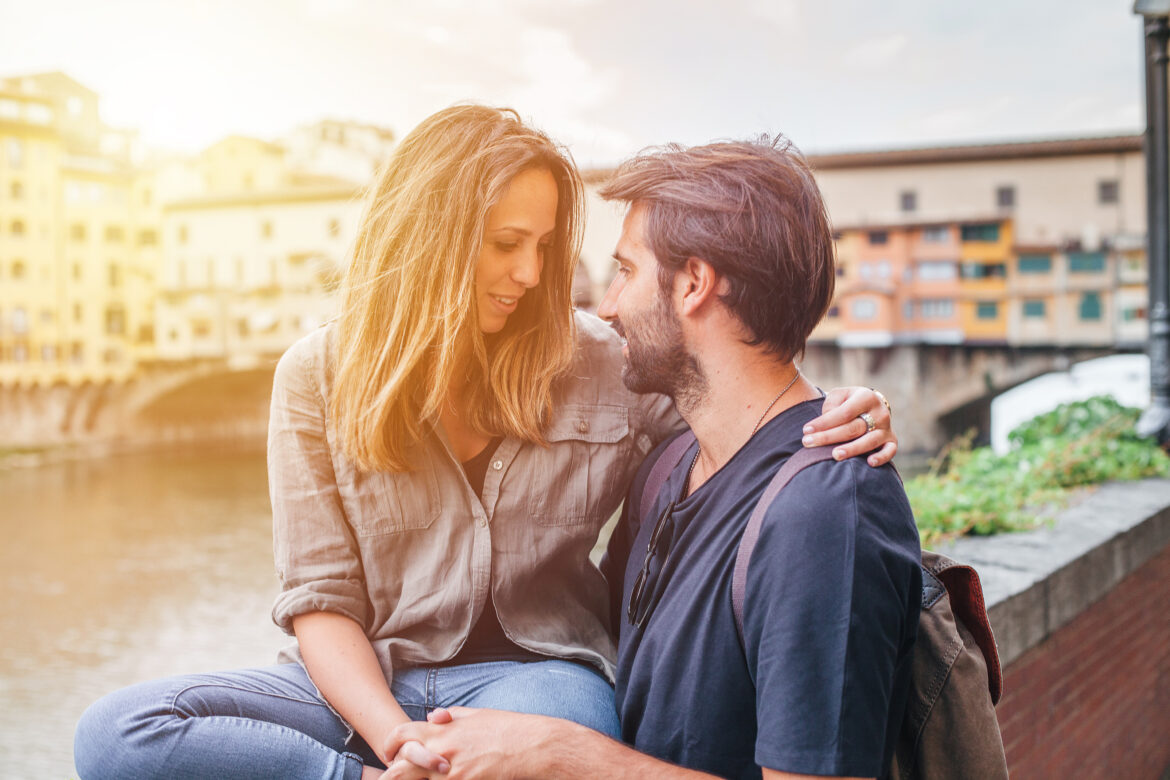 Young couple in love embraces each other in front of Ponte Vecchio in Florence at sunset – Millennial having fun together – Honeymoon in a famous Italian city